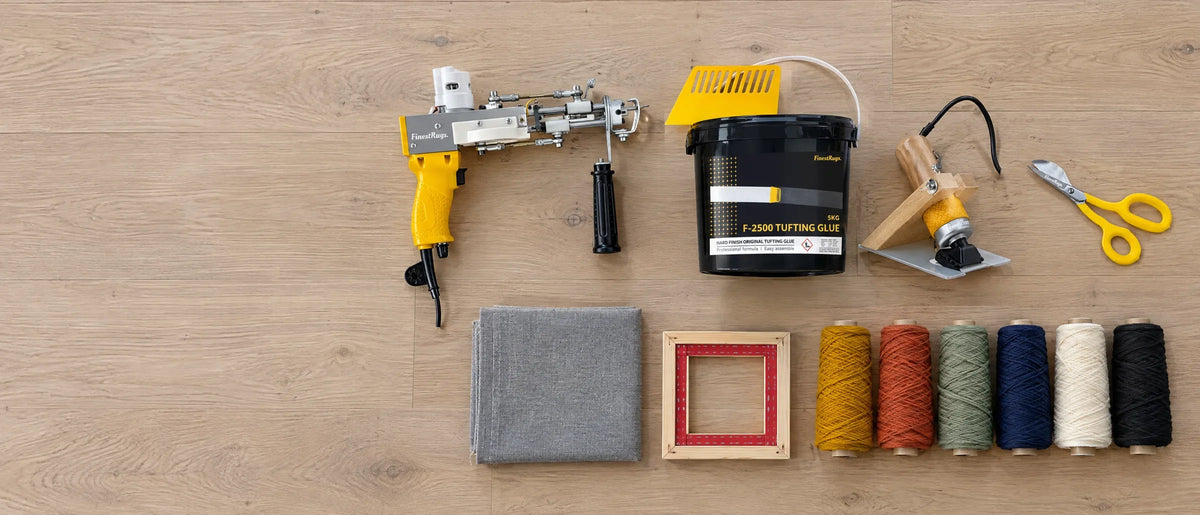Alles wat je nodig hebt om te tuften, van bovenaf op een lichte vloer: tufting gun, lijm, trimmer, schaar, doek en wol
