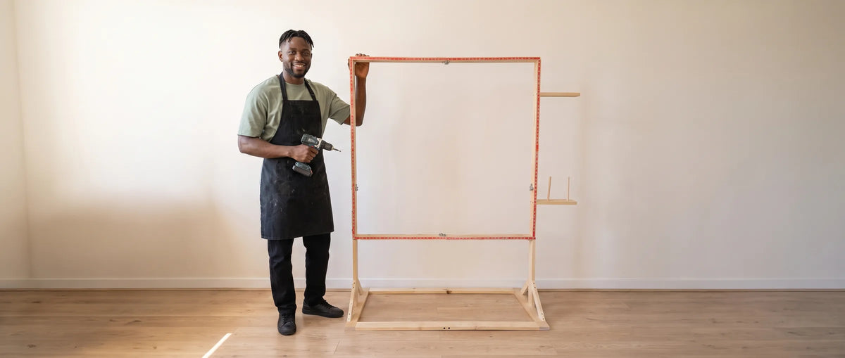 Man staat naast een leeg, staand tufting frame van hout met carpet grippers in een lichte ruimte