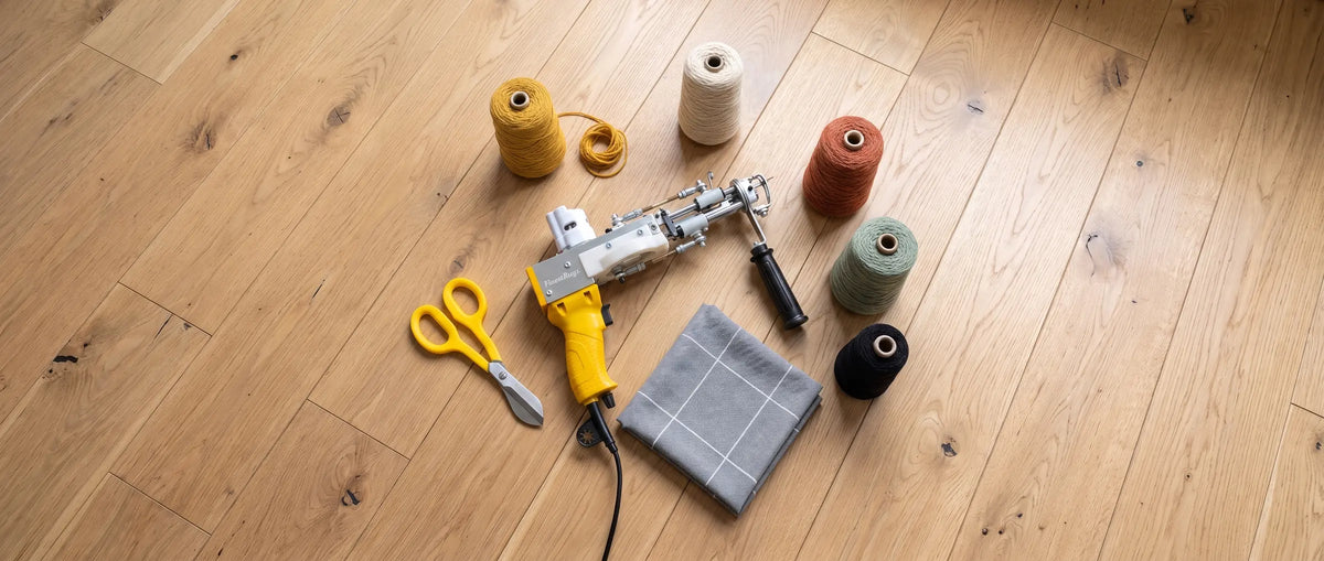 Gele AK-DUO PRO tufting gun op een houten vloer met een schaar, gevouwen tufting doek en vijf kegels wol