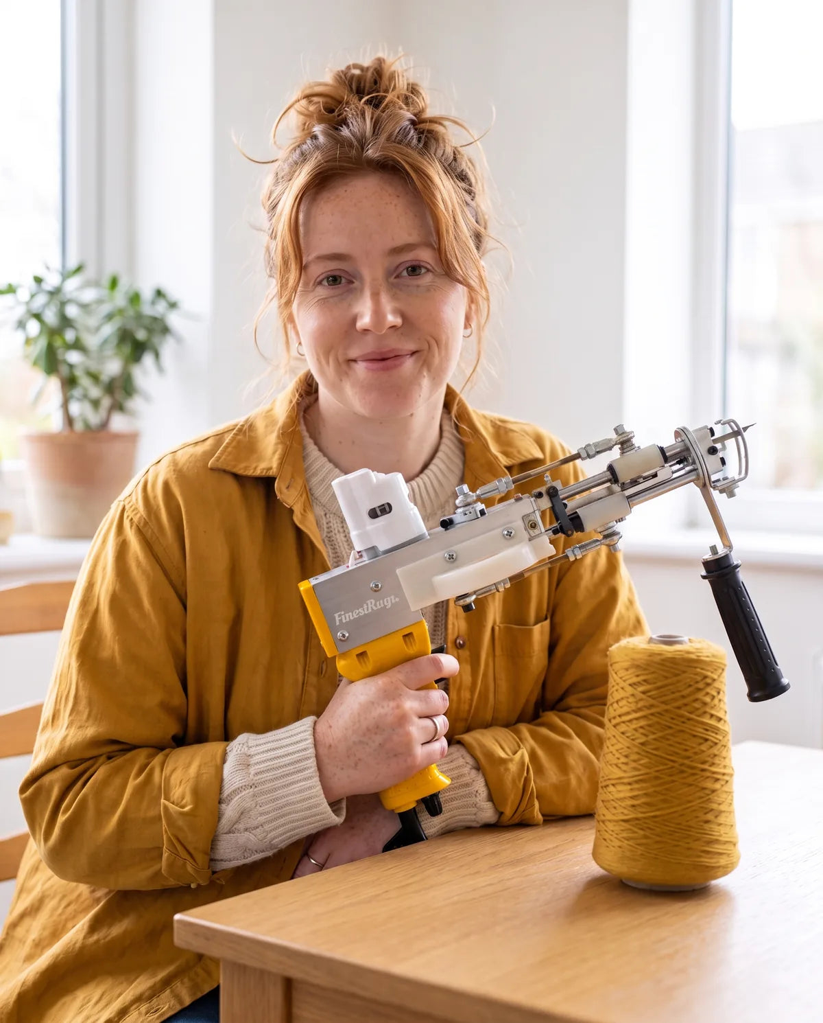 Vrouw aan tafel met de gele AK-DUO PRO tufting gun in de hand en een kegel okergele wol ernaast