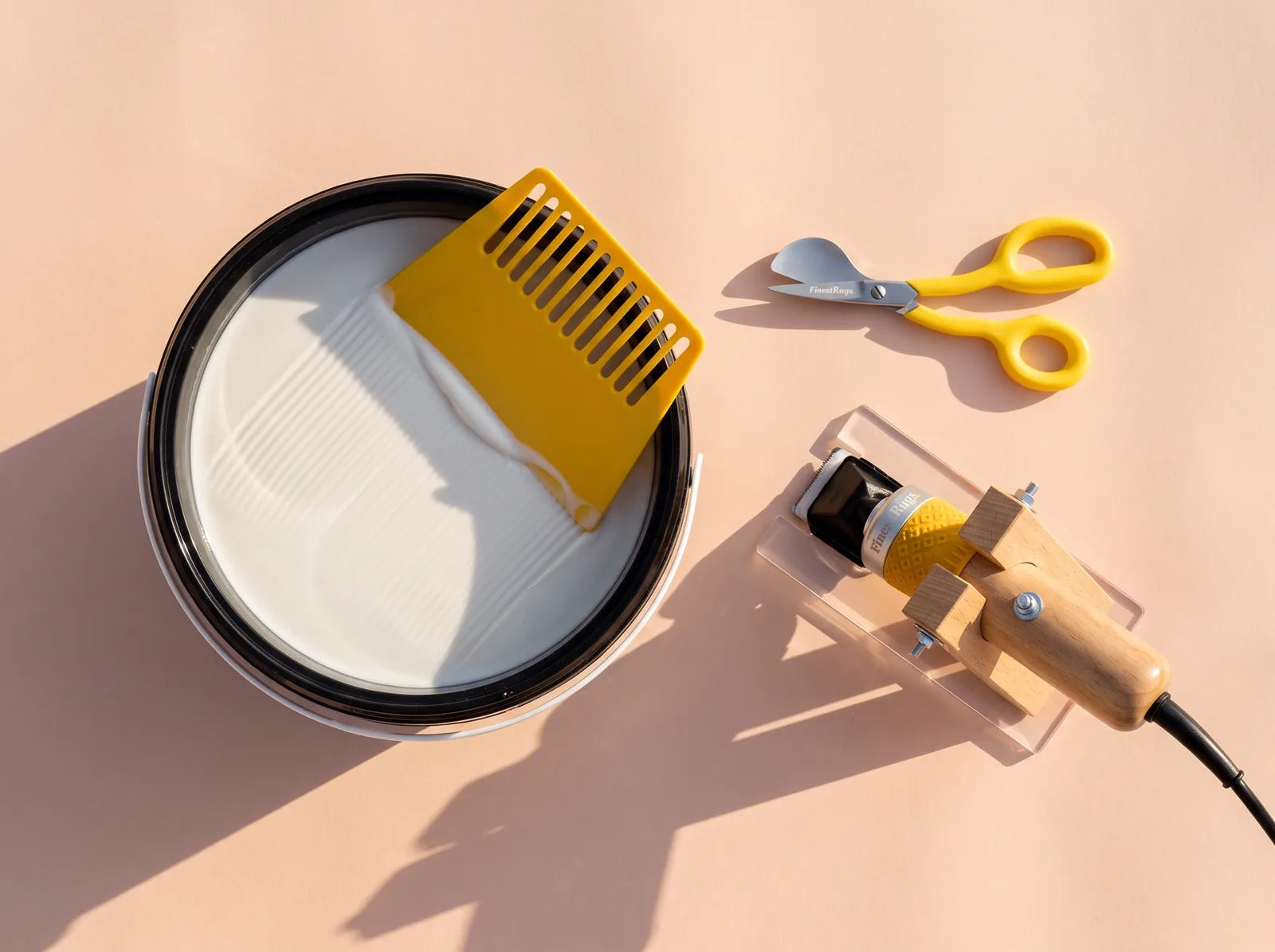 Open emmer latex tufting lijm met een gele lijmkam, naast een tapijt trimmer en een eendenbekschaar, van bovenaf